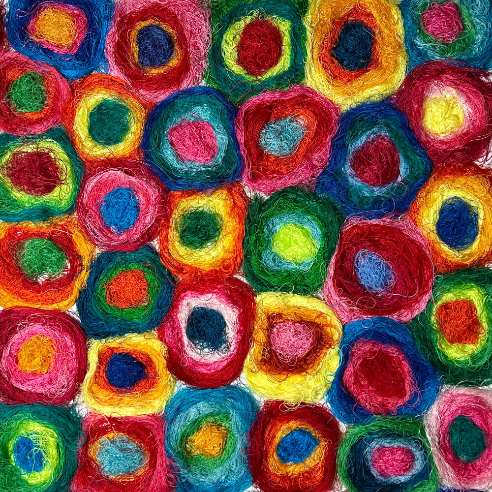 Réalisée à partir de fils colorés enroulés en cercles successifs, elle forme une mosaïque vibrante de couleurs et de matières.