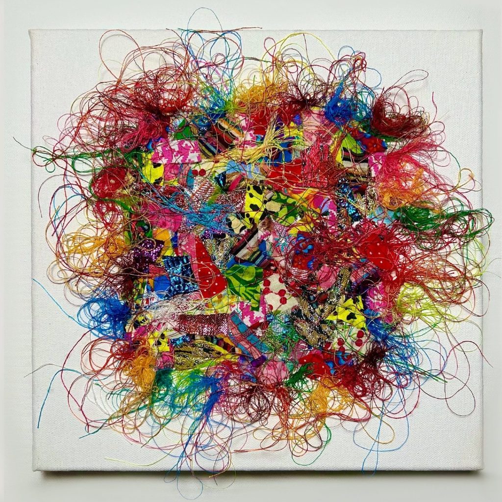 Tableau avec un patchwork de chutes de tissus multicolores composées de motifs variés ainsi que de fils multicolores 100 % coton entremêlés qui débordent en volutes hors du patchwork, orné de quelques sequins sur le dessus de l’oeuvre