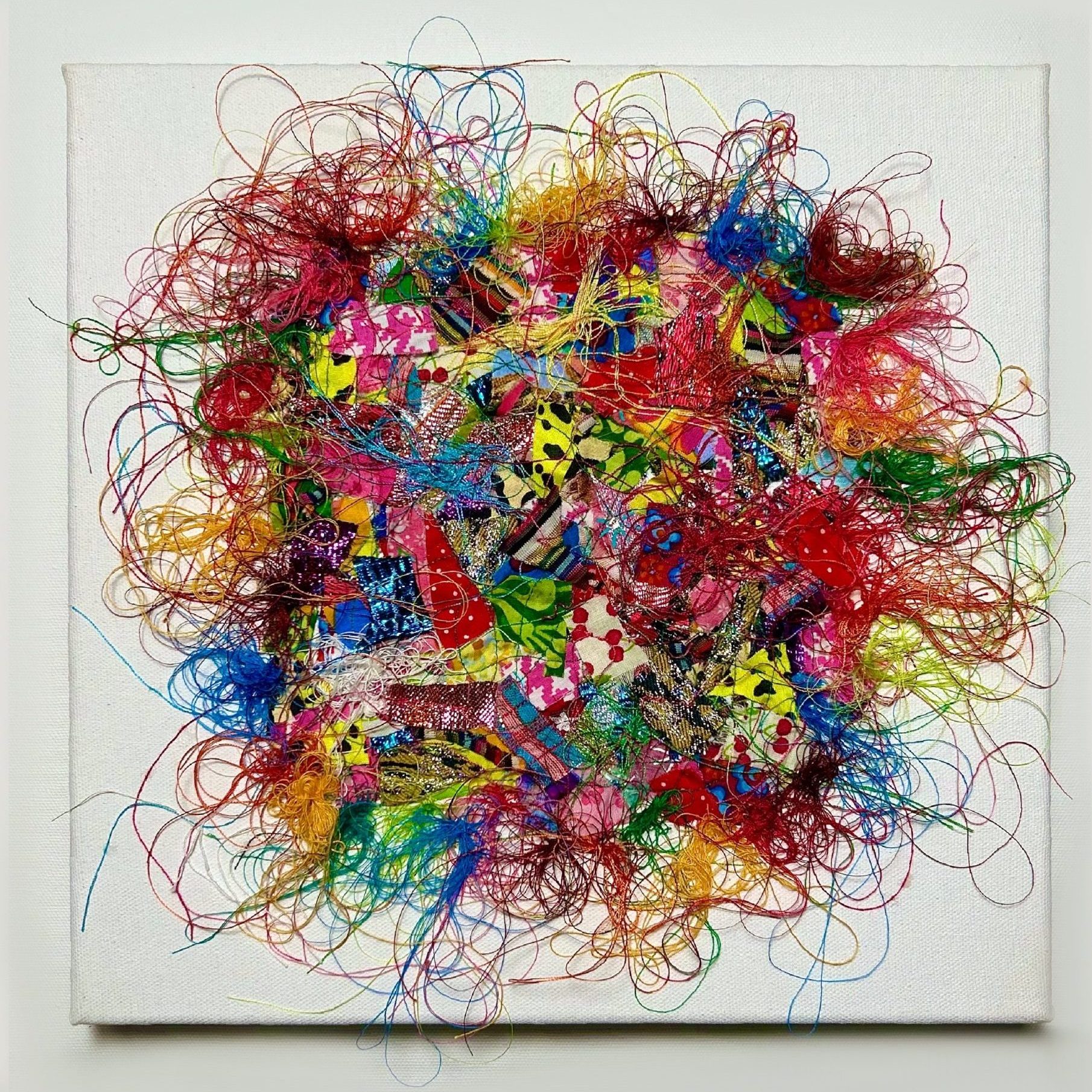 Tableau avec un patchwork de chutes de tissus multicolores composées de motifs variés ainsi que de fils multicolores 100 % coton entremêlés qui débordent en volutes hors du patchwork, orné de quelques sequins sur le dessus de l’oeuvre