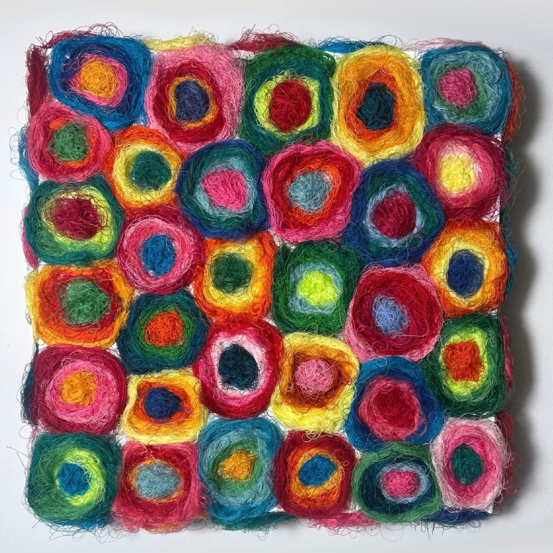 Réalisée à partir de fils colorés enroulés en cercles successifs, elle forme une mosaïque vibrante de couleurs et de matières.